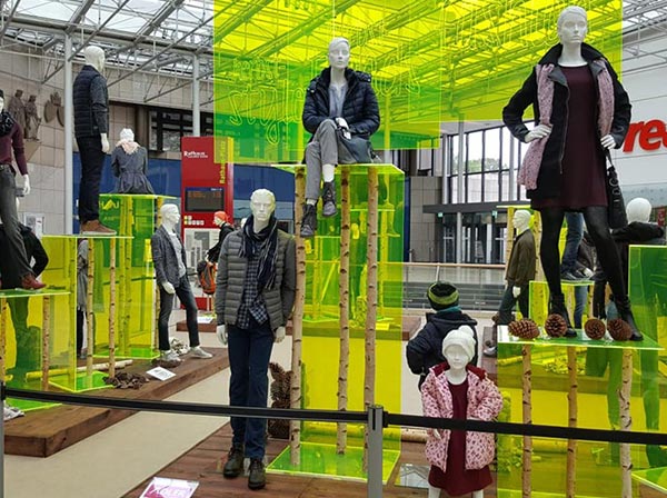 Schaufensterpuppen mit neuer Kleidungskollektion auf hellgrün-transparenten Produktdisplays in einem Einkaufszentrum