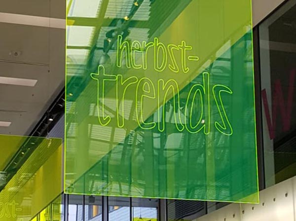 Hängendes Werbeschild aus hellgrün-transperentem Acrylglas mit der Gravur „herbst-trends“