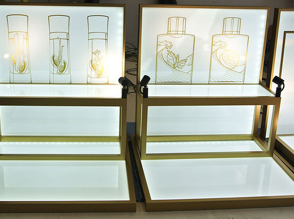 Produktdisplays aus Acrylglas in weiß mit goldenem Rand und gemalten Produktbildern im Hintergrund mit direkter und indirekter Beleuchtung