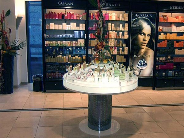 Runder Tisch aus Acryglas mit Metall-Sockel und indirekter Beleuchtung in einem Geschäft für Kosmetikartikel, auf dem Parfümflaschen und Dekoration ausgestellt ist