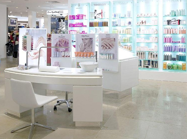 Einrichtung eines Geschäfts für Kosmetikartikel mit beleuchteten Regalen, Produktdisplays und einem Tisch aus Acrylglas für die Nagelpflege aus