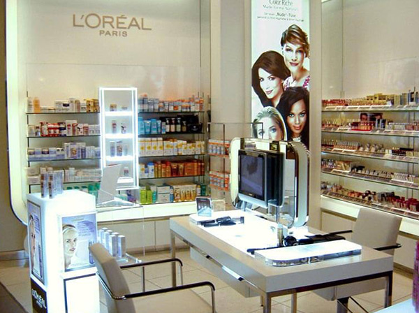 Beleuchtete Ladeneinrichtung mit Schminktisch, Regalen für Kosmetikartikel und Schriftzug von L`Oréal an der Wand aus Acrylglas