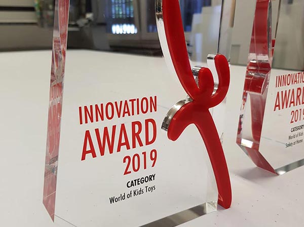 Award aus farblos, transparentem und roten Plexiglas mit der Beschriftung „Innovation Award 2019 Category World of Kids Toys“ und dem „Kind+Jugend“-Logo