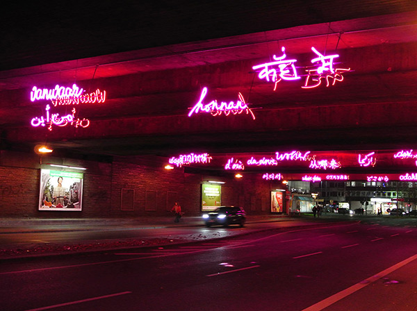 Leuchtschrift unter einer Brücke in rot in verschiedenen Sprachen
